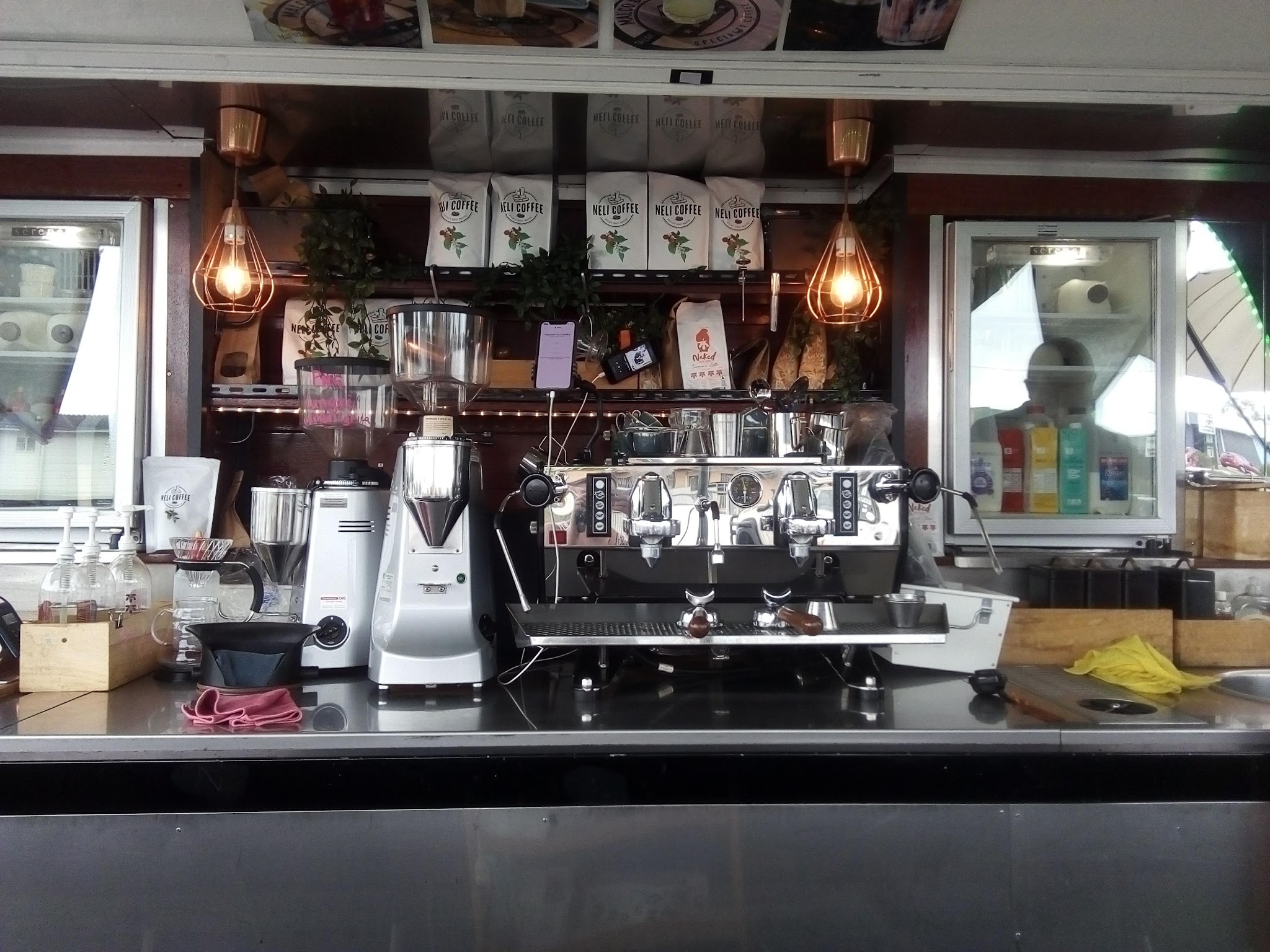 The espresso machine and grinders inside the bar, lit by copper pendant lights with coffee bags on the shelves