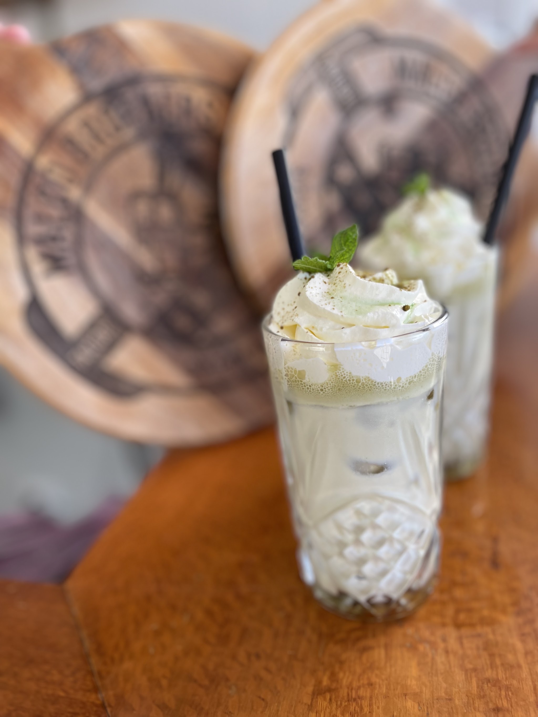 An iced drink topped with whipped cream and mint on a wood-burned MALCO Brothers serving board