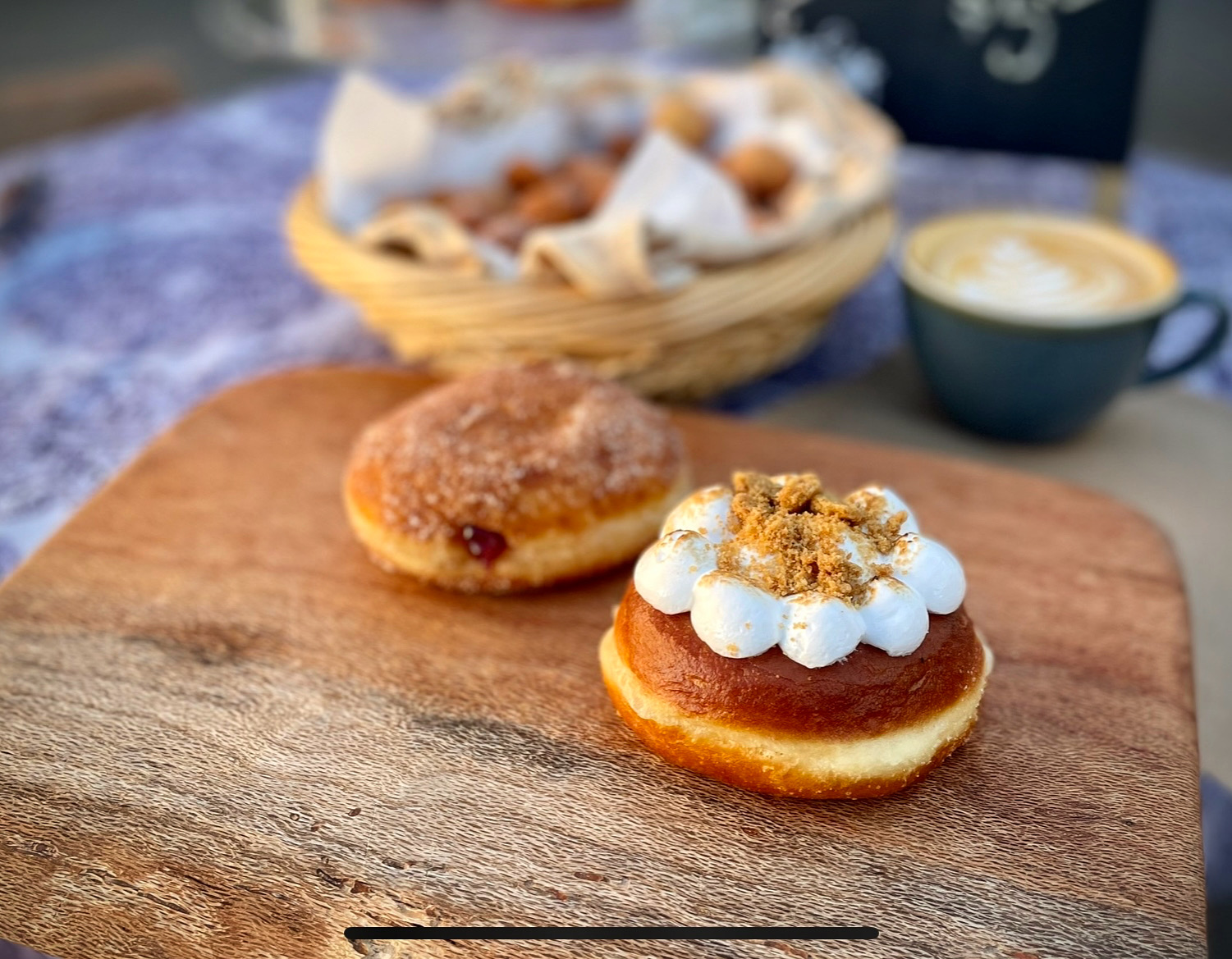 A cinnamon sugar donut and a toasted brioche donut with a coffee behind them