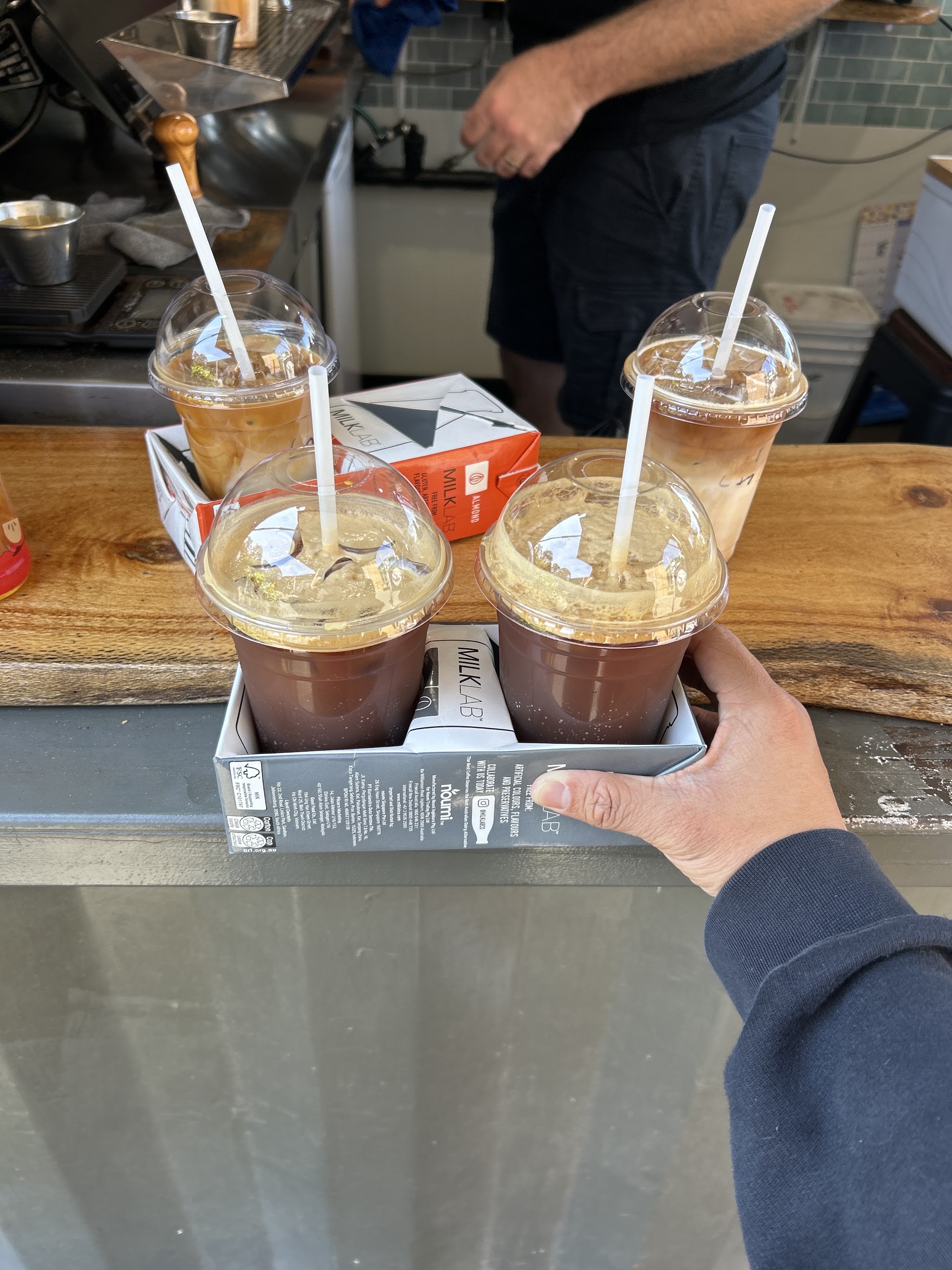 A hand holding a carrier of four iced coffees and hot chocolates